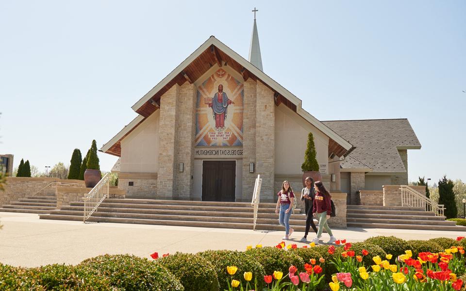 photo of three female students walking in front of Our Lady of Perpetual Help Chapel