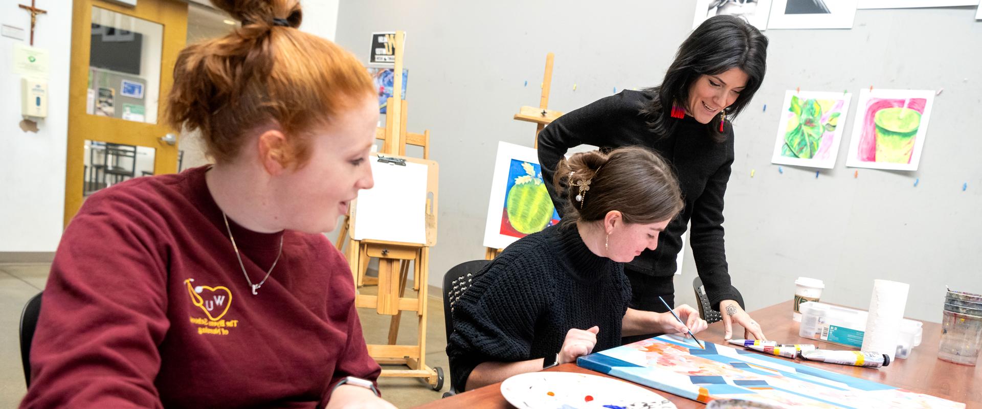 photo of two students in a painting class being observed by the instructor